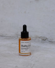 Load image into Gallery viewer, A small glass dropper bottle of Dewy Monday Baby Face Serum with amber liquid, a white label, and a black dropper cap, set against a textured light gray background.